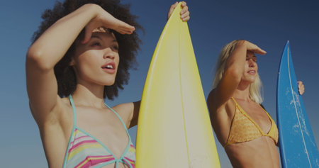 Diverse couple with surfboards at the beach, with copy space. They're enjoying a sunny day by...