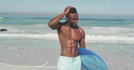 Young African American man enjoys a sunny beach day, with copy space. He&#39;s ready for surfing, highlighting a healthy, active lifestyle.の写真素材