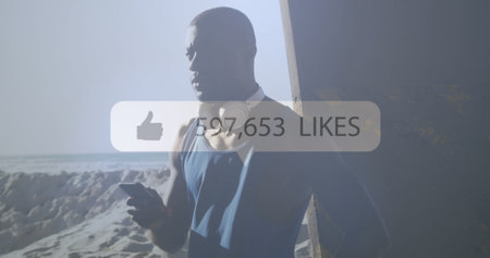 Speech bubble with increasing likes against african american fit man using smartphone at the beach. sports, fitness and social media networking technology conceptの写真素材