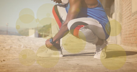 Yellow spots of light against mid section of african american fit man tying shoe laces at the beach....