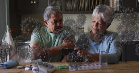 Image of covid 19 cells over senior couple using smartphone at home. global covid 19 pandemic, health and medicine concept digitally generated image.の写真素材
