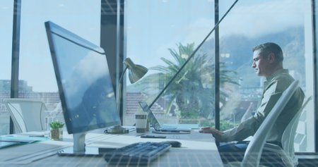 Caucasian businessman works at a desk in a bright office. He is focused on his computer screen, suggesting productivity in a corporate environment.の写真素材