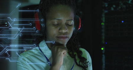 Image of integrated circuit over african american woman working on laptop in server room. network,...