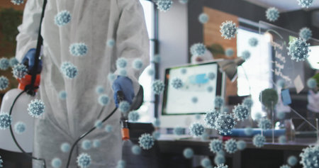 Multiple covid-19 cells floating against male health worker spraying disinfectant at office. cleaning and disinfection infection prevention and control of covid-19 epidemicの写真素材