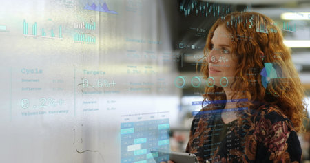 Image of financial data with icons over caucasian businesswoman in office. Global business, finances, computing and data processing concept digitally generated image.の写真素材