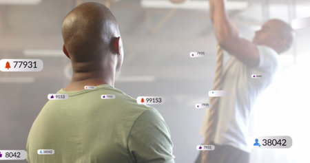 Image of social media notifications over diverse male trainer and man climbing rope at gym. Fitness,...