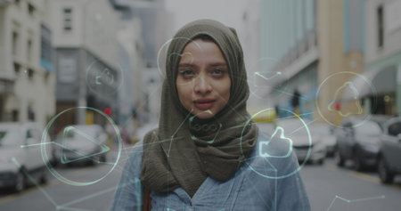 Image of connected media icons with smiling woman wearing hijab walking in street. communication technology digital interface concept, digitally generated image. mediaの写真素材