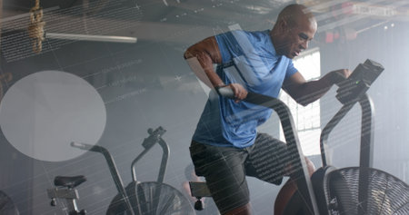 Image of data on interface over african american man cross training on elliptical at gym. Fitness,...