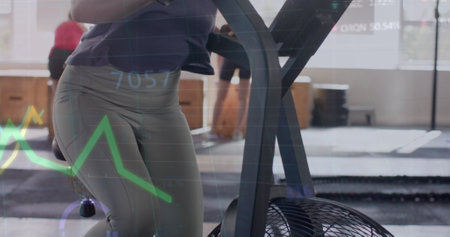 Image of data on graph over caucasian woman cross training on elliptical at gym. Fitness, exercise,...