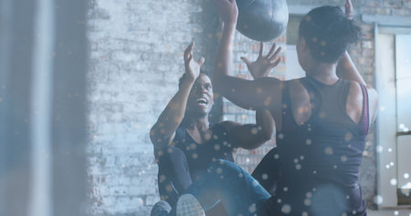White particles floating against african american man and woman working out with medicine ball. sports and fitness conceptの写真素材