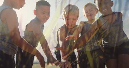 Image of sun and grasses over happy diverse schoolchildren stacking hands in outdoor sport class....