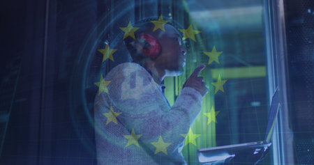 Image of eu flag over african american man using laptop in server room. Cloud computing, digital interface and security concept digitally generated image.の写真素材