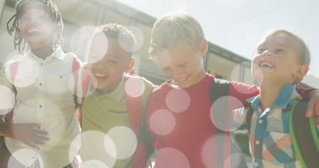 Image of bokeh lights over happy diverse schoolboys walking together outside school. Friendship, school, education, childhood and learning, digitally generated image.の写真素材