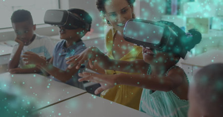 Image of particles of light over diverse female teacher and pupils in vr headsets in classroom. Digital interface, school, education, childhood and learning, digitally generated image.の写真素材