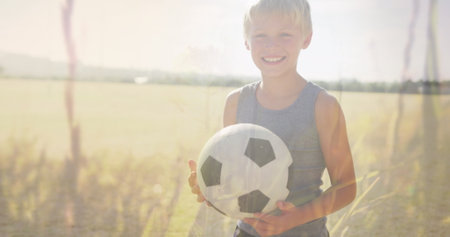 Image of plants and sunlight over happy caucasian schoolboy with football in field. Sport, health, school, education, childhood and learning, digitally generated image.の写真素材