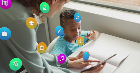 Image of school icons over diverse female teacher with tablet talking to schoolboy at desk....