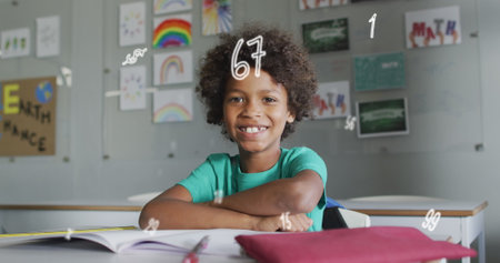 Image of numbers over happy biracial schoolboy sitting at desk in class smiling. Communication, technology, school, education, childhood and learning, digitally generated image.の写真素材