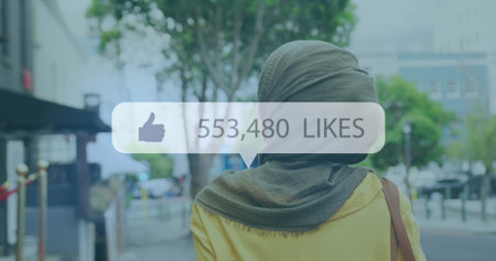 Image of like symbol with rising number and woman in hijab wheeling bike in city street. communication technology digital interface concept, digitally generated image.の写真素材