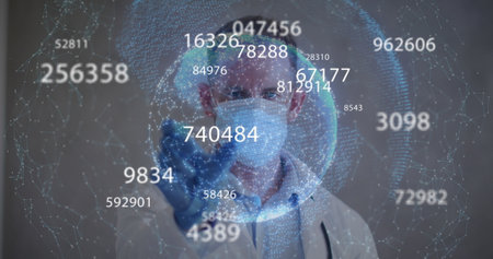 Image of statistics recording and globe over male doctor wearing gloves and face mask. global covid 19 pandemic, health and medicine concept digitally generated image.の写真素材