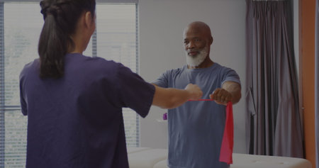 Senior African American man exercises with a therapist at a rehabilitation center. They focus on...