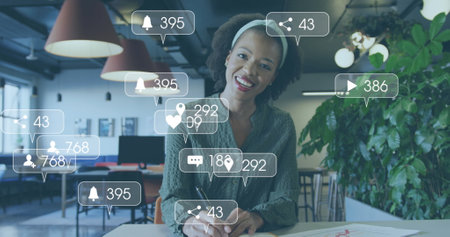 Image of social media icons with numbers over african american businesswoman working at office. Global business and digital interface concept digitally generated image.の写真素材