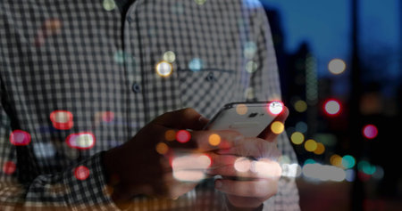 Spots of colorful bokeh lights against mid section of man using smartphone on the street. global networking and technology conceptの写真素材