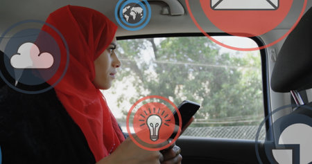Multiple digital icons floating against woman in hijab using smartphone in the car. global...