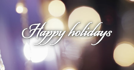 Image of happy holidays text over yellow spots of light background. Christmas, tradition and celebration concept digitally generated image.の写真素材