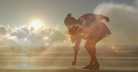 Woman picking up an item on a beach with clouds above.