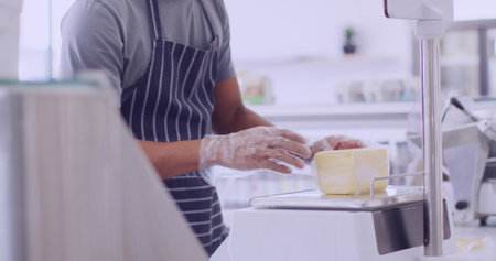 African American man slices cheese in a bright kitchen. He works meticulously, suggesting a...