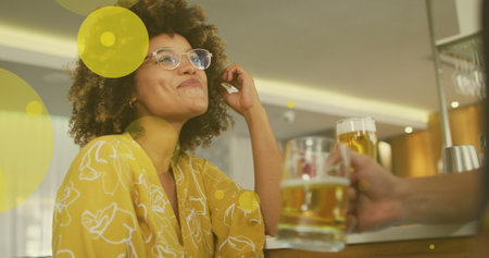 Image of spots over happy biracial woman with caucasian friend drinking beer. social media and communication interface concept digitally generated image.の写真素材