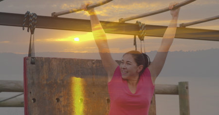 Image of sunset over caucasian woman at obstacle course hanging. Global sport, health, fitness and...