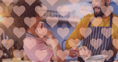 Image of hearts over diverse couple preparing meal in kitchen. Relationship, love, romance and...