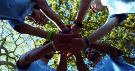 Diverse group of volunteers stack hands outdoors, with copy space. Teamwork and community service are emphasized in this sunny, outdoor setting.の写真素材