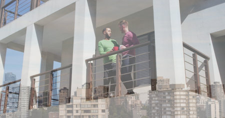 Image of cityscape over diverse male couple standing on balcony and drinking coffee. Valentine&#39;s day, love and celebration concept digitally generated image.の写真素材