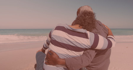 Rear view of african american couple hugging each other while sitting at the beach. Travel vacation retirement lifestyle conceptの写真素材