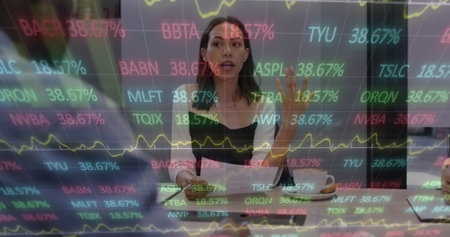 Image of financial data and graphs over biracial woman in office. Business, finance, economy, cooperation and communication concept digitally generated image.の写真素材