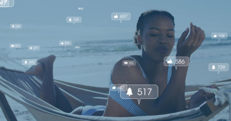 Image of social media reactions over happy african american woman in hammock on beach. Holidays, vacations and relax concept digitally generated image.の写真素材