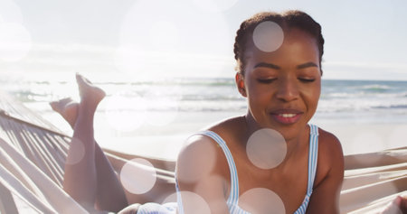Image of dots over happy african american woman in hammock on beach. Holidays, vacations and relax concept digitally generated image.の写真素材