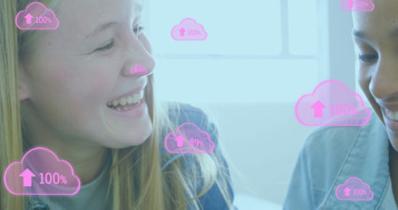 Image of digital cloud icons over two female students smiling and working together. Education...