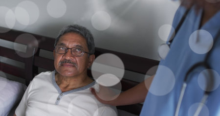 Image of light spots over diverse doctor and patient talking and holding hand. Medicine, healthcare and lifestyle concept digitally generated image.の写真素材