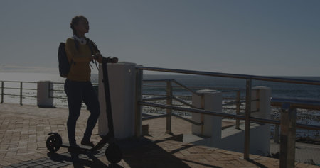 Image of financial data processing over biracial woman walking with e scooter. global travel,...