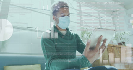 Image of statistics processing over businessman wearing face mask using tablet in office. global...