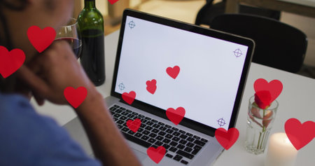 Image of hearts over biracial man drinking wine and using laptop with copy space. Valentines day and celebration concept digitally generated image.の写真素材