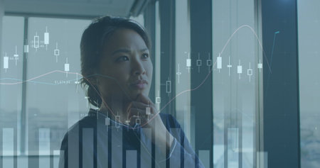 Image of multiple graphs over thoughtful asian woman with hand on chin looking away in office. Digital composite, multiple exposure, report, business, contemplation and technology concept.の写真素材