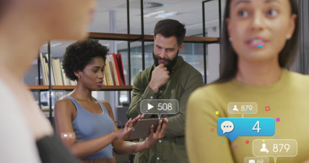 Image of social media icons over diverse man and woman discussing over digital tablet at office. Social media networking and business technology conceptの写真素材