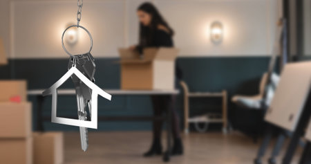 Image of hanging golden house keys against blurred view of woman unpacking boxes. Relocation and real estate conceptの写真素材