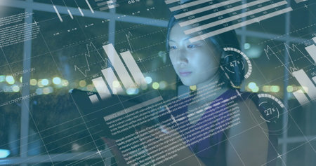 Asian woman, 22, wearing glasses, examining digital data on transparent screen. She has long black...