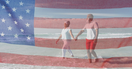Diverse couple holding hands, walking on beach with blue background. Both seniors, wearing casual summer clothes, enjoying sunshineの写真素材