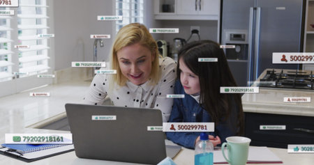 Caucasian mother and daughter, wearing casual clothes, studying laptop in kitchen. Mother with...